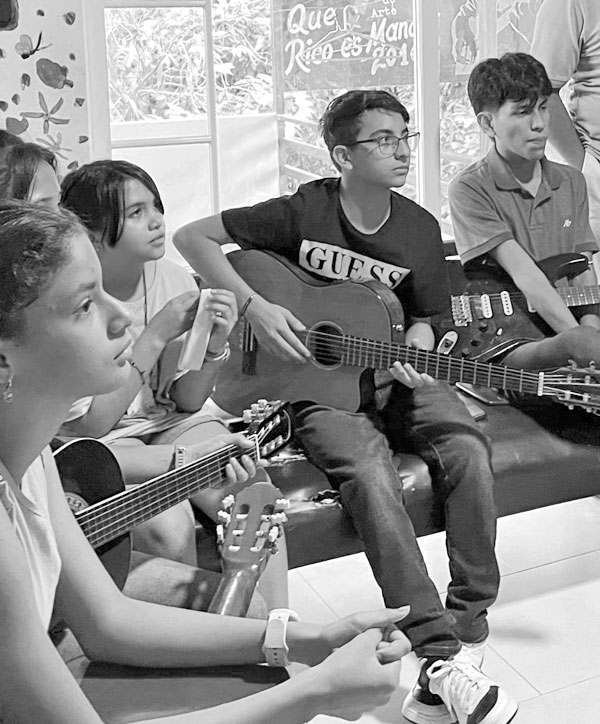 Jóvenes tocan guitarra sentados en círculo durante una clase de música de la Fundación Visión Raíces, fotografía en blanco y negro