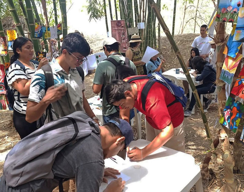 Jóvenes se registran en una mesa durante el evento Slow Food, rodeados de bambú y pinturas colgadas, Fundación Visión Raíces